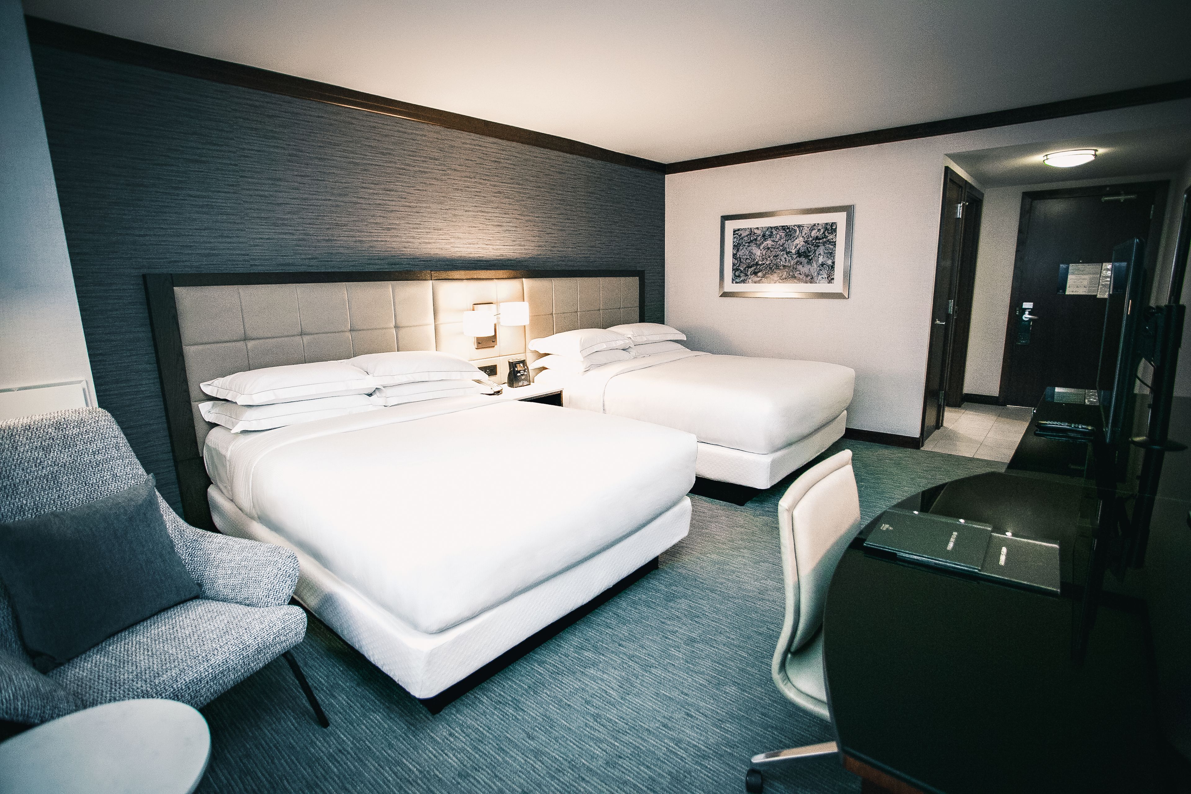 A hotel room with two beds, a desk, a chair, and a small table.