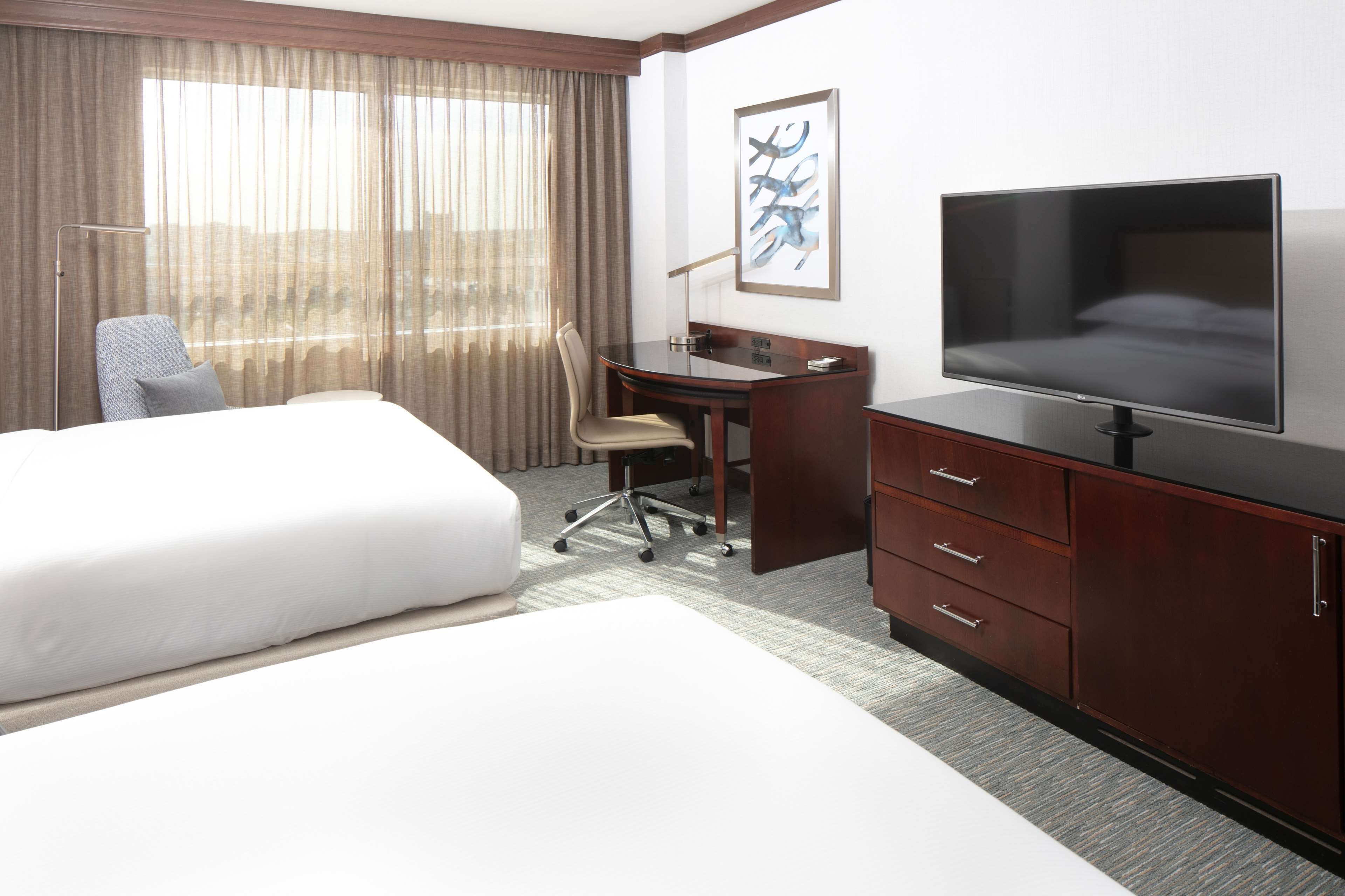 A hotel room with a large bed, a desk with a chair, a television, and a window with curtains.