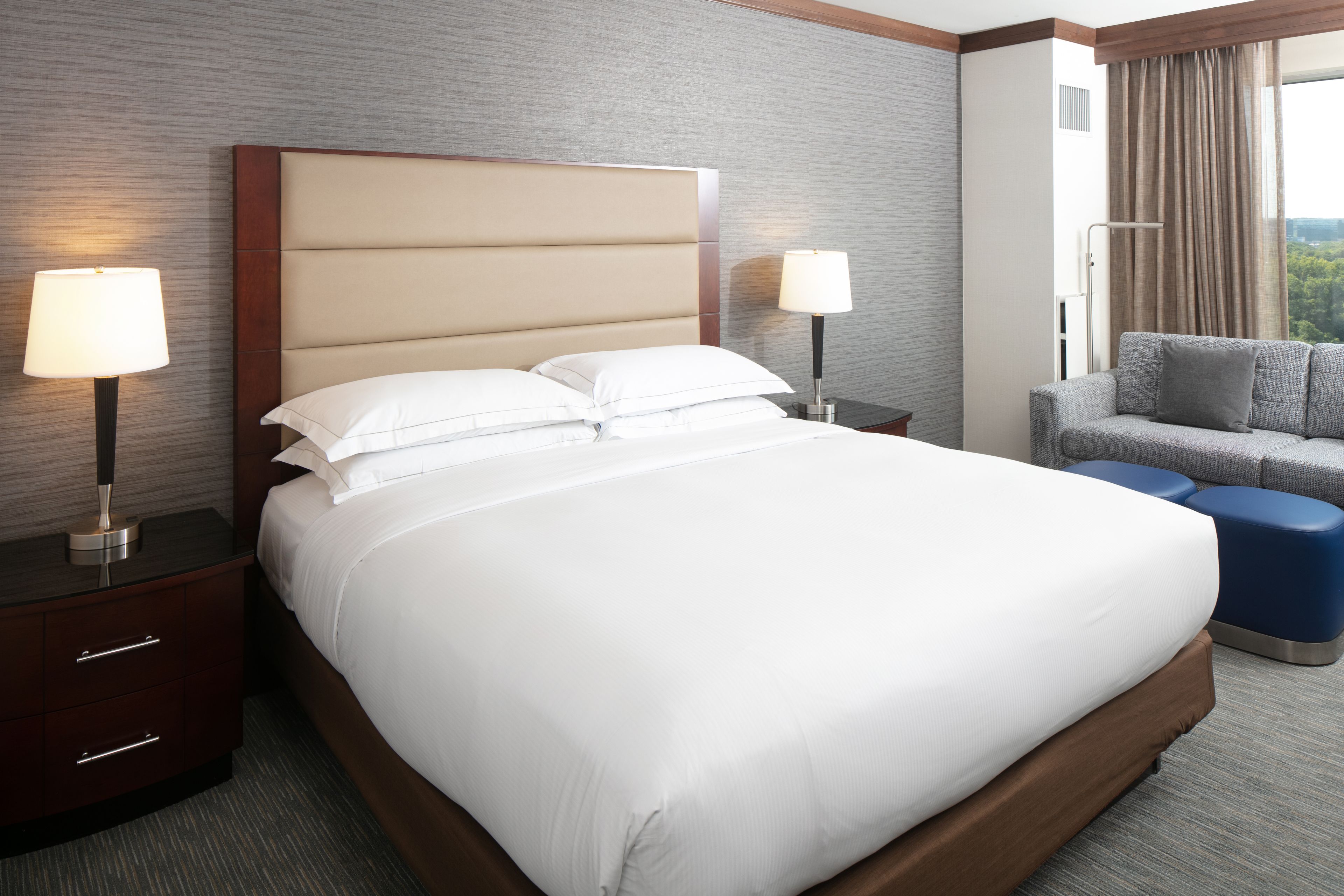 A neatly made bed with white linens, a wooden headboard, and two bedside lamps.