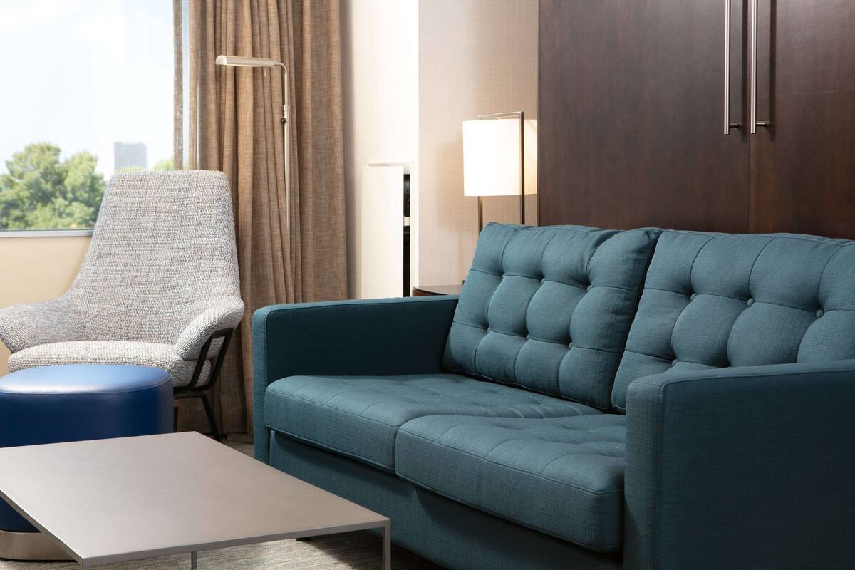 A modern hotel room with a blue sofa, a grey armchair, and a small table.