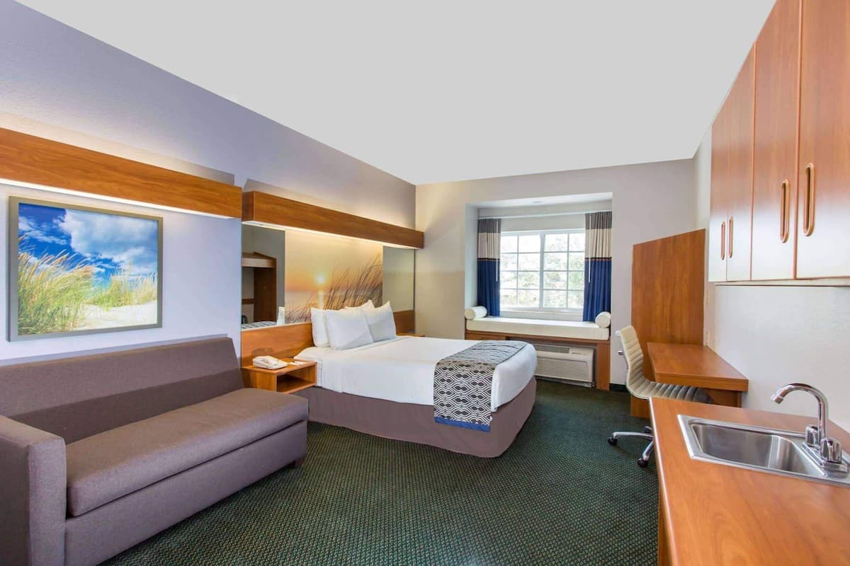 Una habitación de hotel con cama, sofá, escritorio, ventana y kitchenette.
