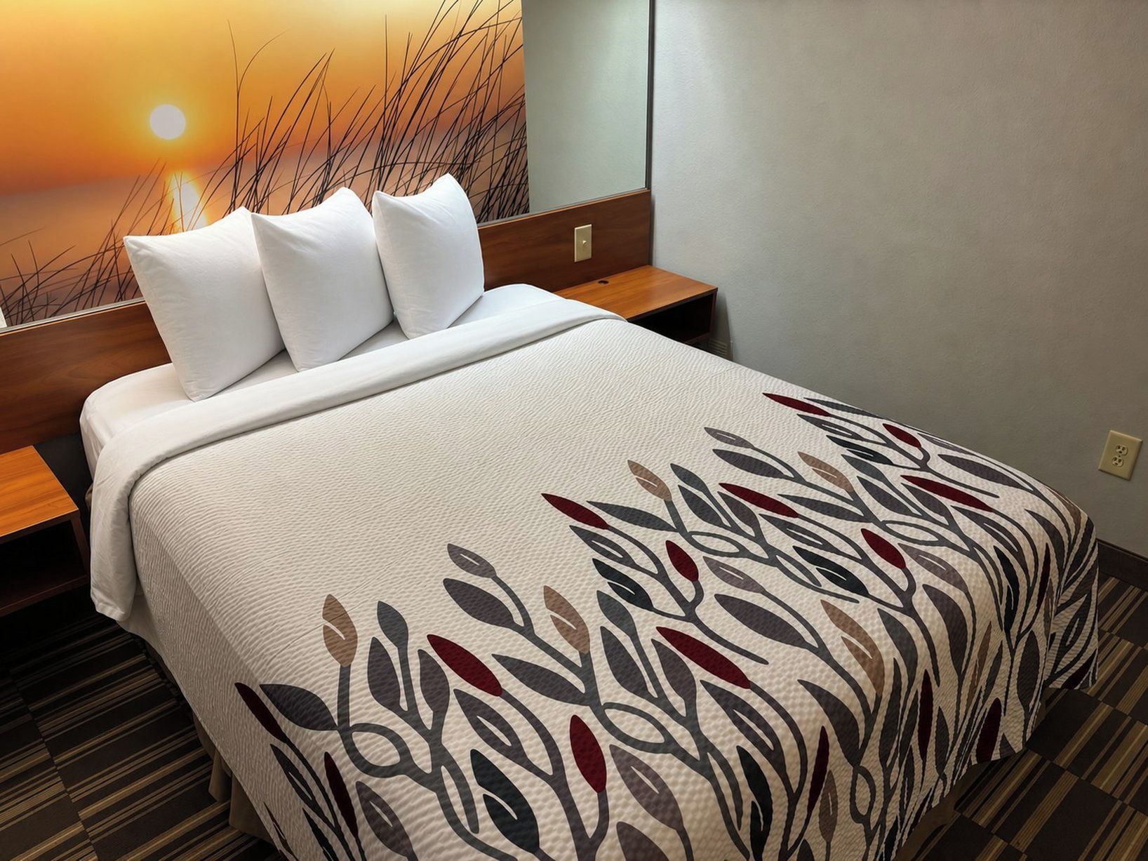 A hotel room with a bed, white pillows, a patterned bedspread, a nightstand, and a wall with a sunset view.