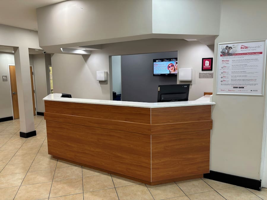 Uma mesa de recepção com acabamento em madeira, um monitor de tela plana acima e um cartaz promocional do RediRewards na parede.
