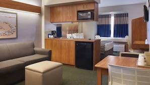 A compact hotel room with a kitchenette, a sofa, a dining table, and a bed. - Microtel Inn & Suites by Wyndham Port Charlotte/Punta Gorda (Port Charlotte)
