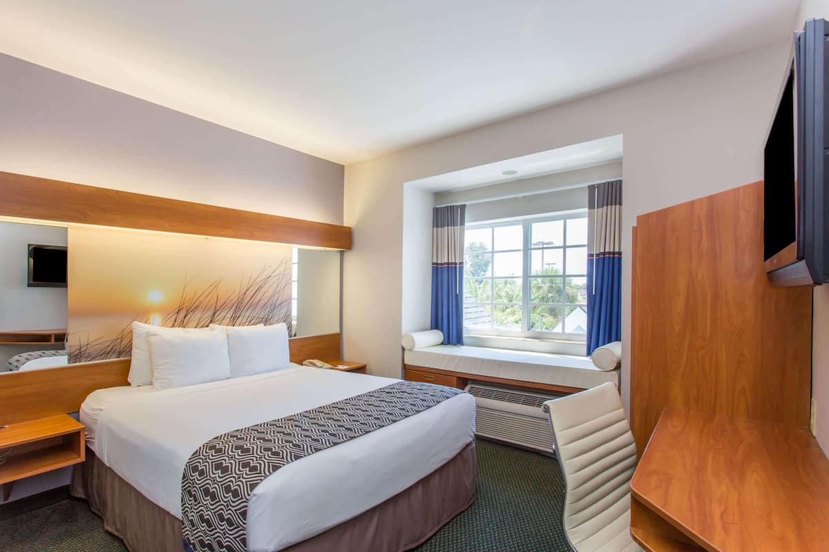 Habitación de hotel con una cama grande, un escritorio, una silla, un televisor y una ventana con cortinas.