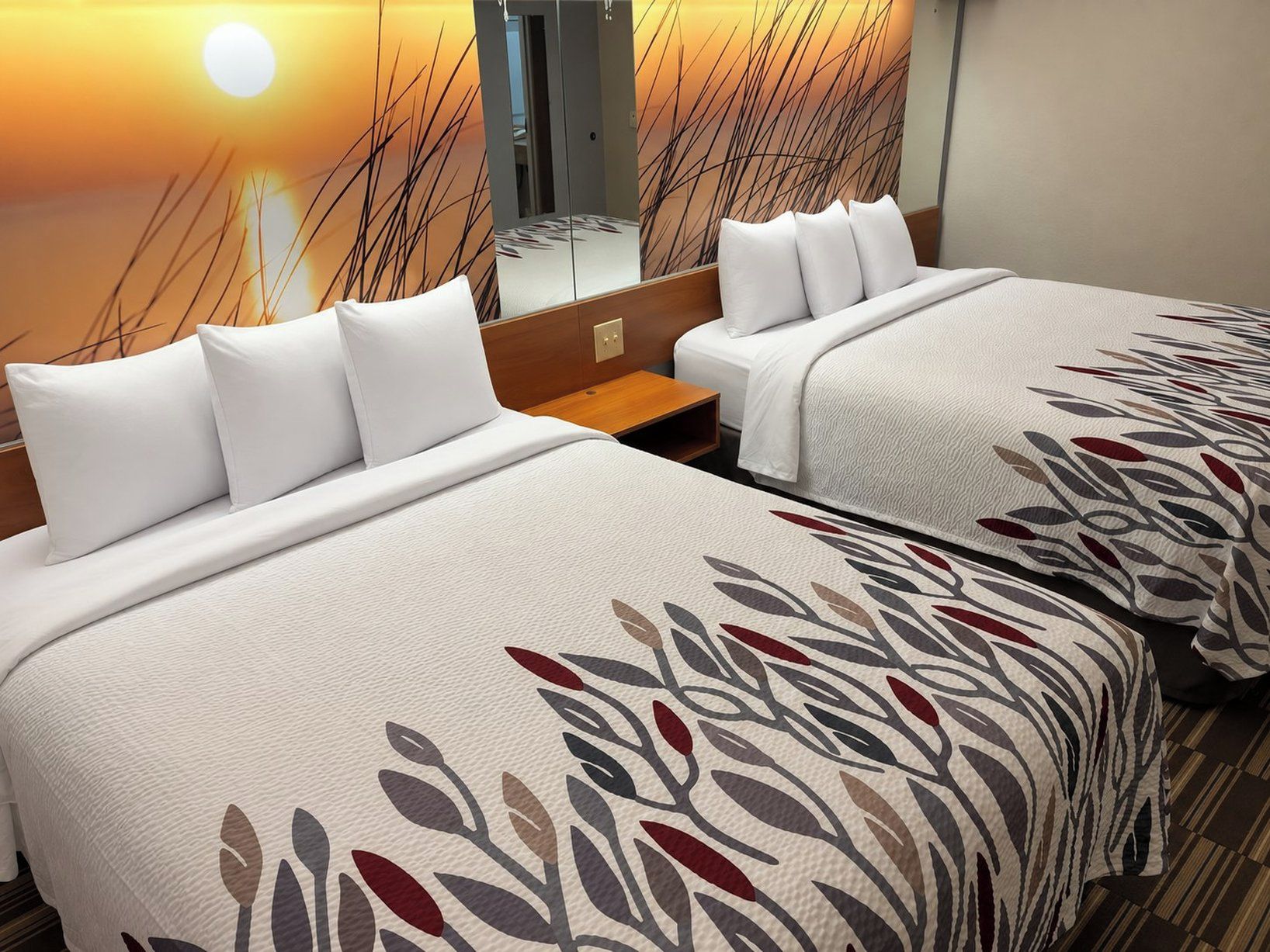 A hotel room with two beds, each with white bedding and a leaf-patterned throw.