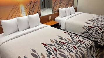 A hotel room with two beds, each with white bedding and a leaf-patterned throw.