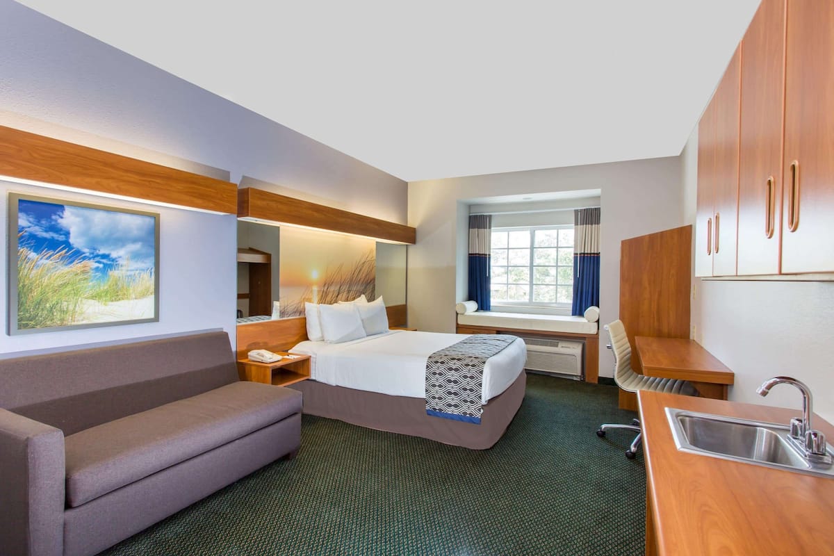 Habitación de hotel con cama, sofá, escritorio, lavabo y ventana con cortinas.