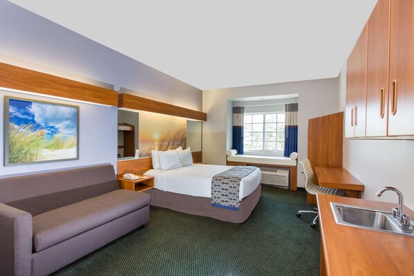 Quarto de hotel com cama, sofá, escrivaninha, pia e janela com cortinas.