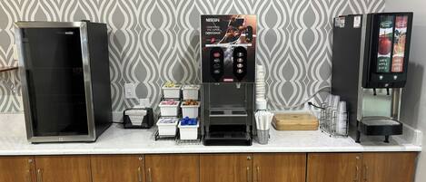 Una estación de café con máquina de Nescafé, un refrigerador y un dispensador de jugo.