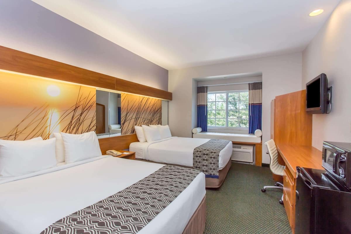 Una habitación de hotel con dos camas, un escritorio, un televisor y una ventana con cortinas.
