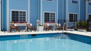 A pool area with lounge chairs and flower arrangements, surrounded by a building with blue siding and multiple windows. - Microtel Inn & Suites by Wyndham Port Charlotte/Punta Gorda (Port Charlotte)