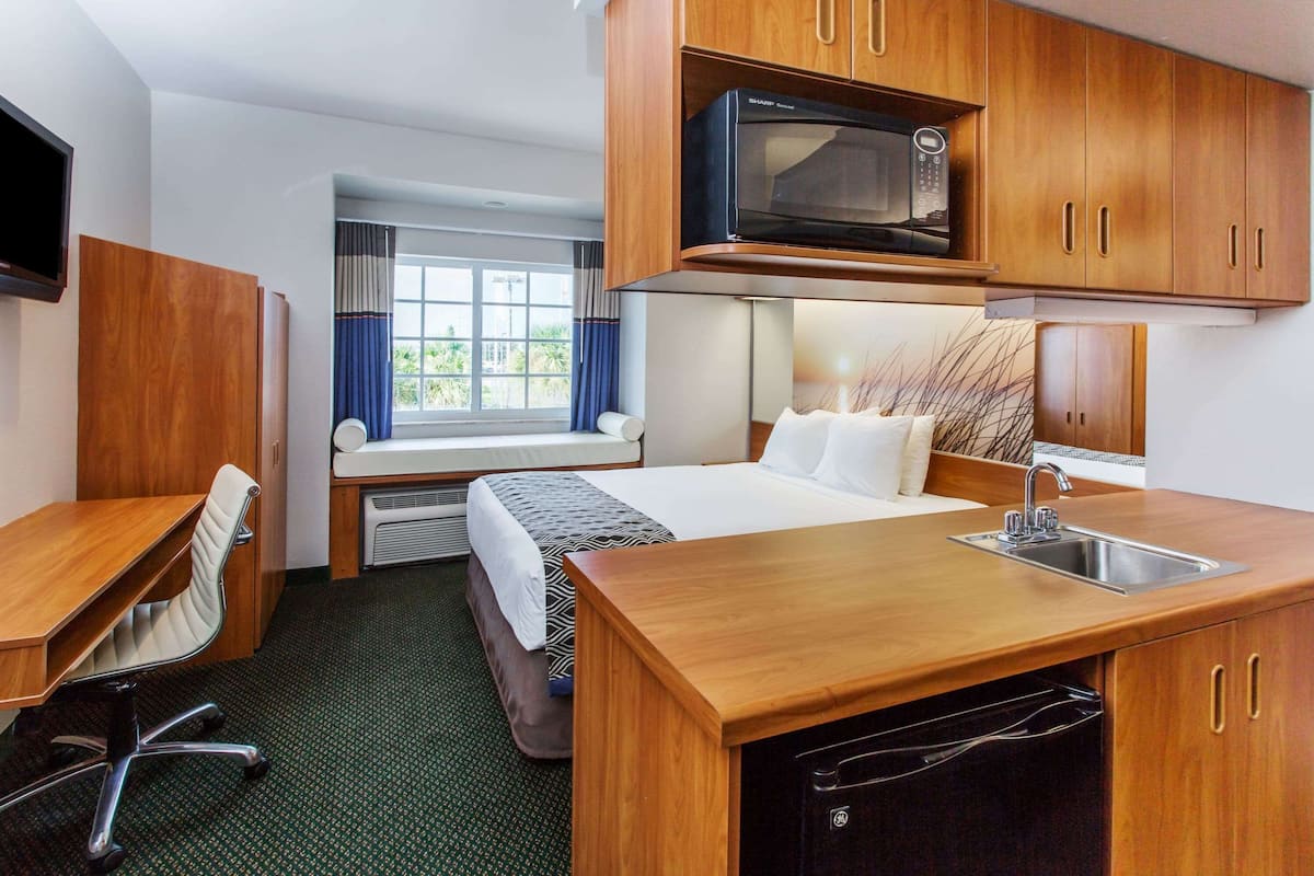 Habitación de hotel con kitchenette, cama, escritorio y ventana con cortinas.