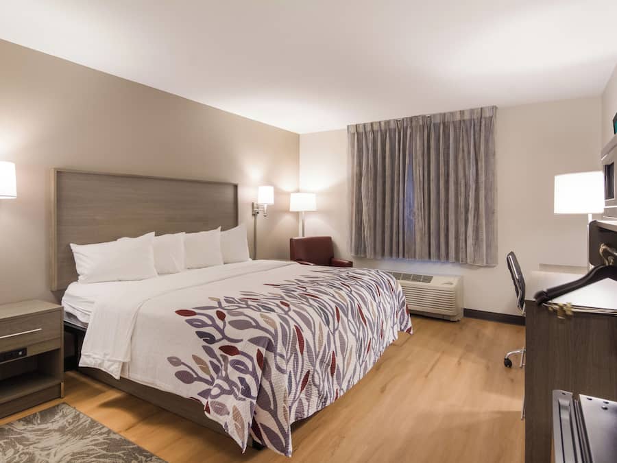 Habitación de hotel con cama, mesitas de noche, escritorio, silla, ventana con cortinas y aire acondicionado.