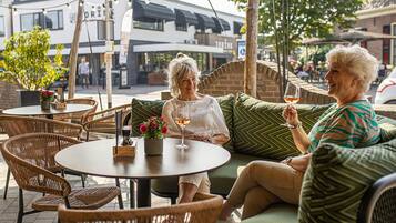 An outdoor seating area with wicker chairs and tables, a potted plant, and a glass of wine.