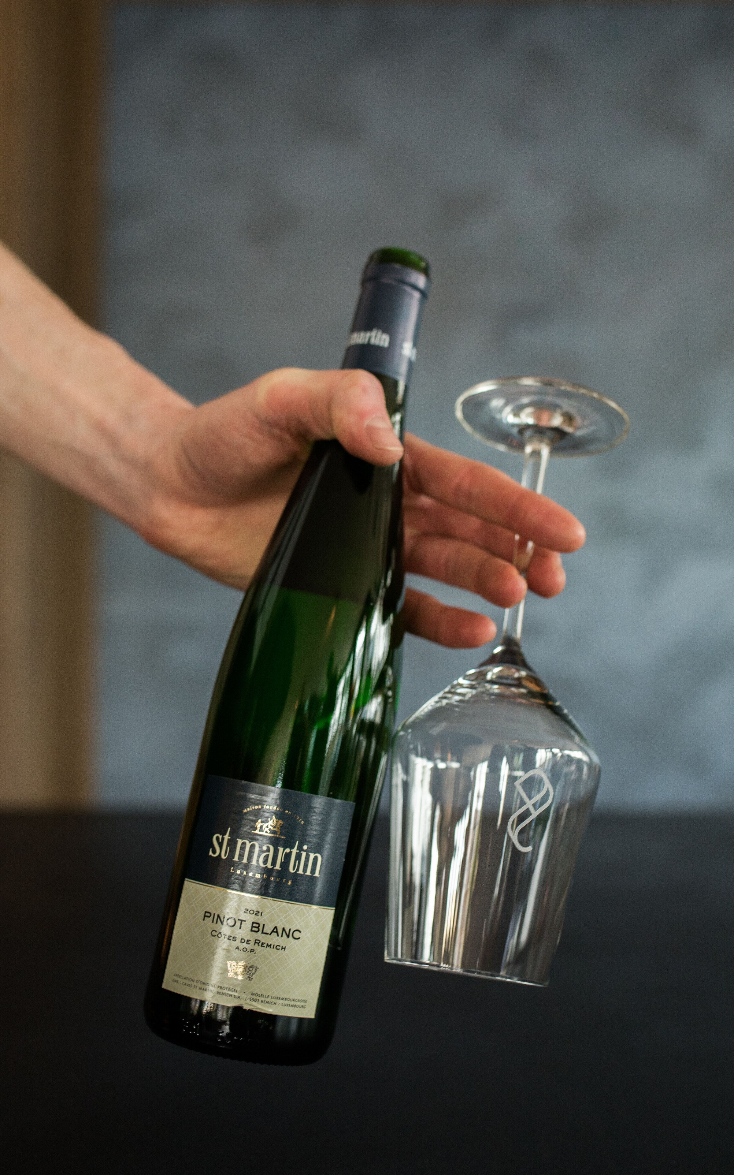 A hand holding a bottle of St. Martin Pinot Blanc wine next to a wine glass.