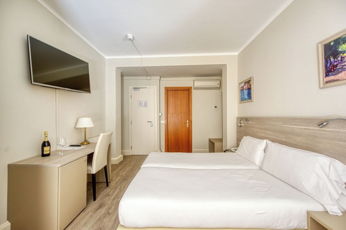 Una habitación de hotel con una cama, un escritorio con una silla, un televisor y una puerta que da a otra habitación.