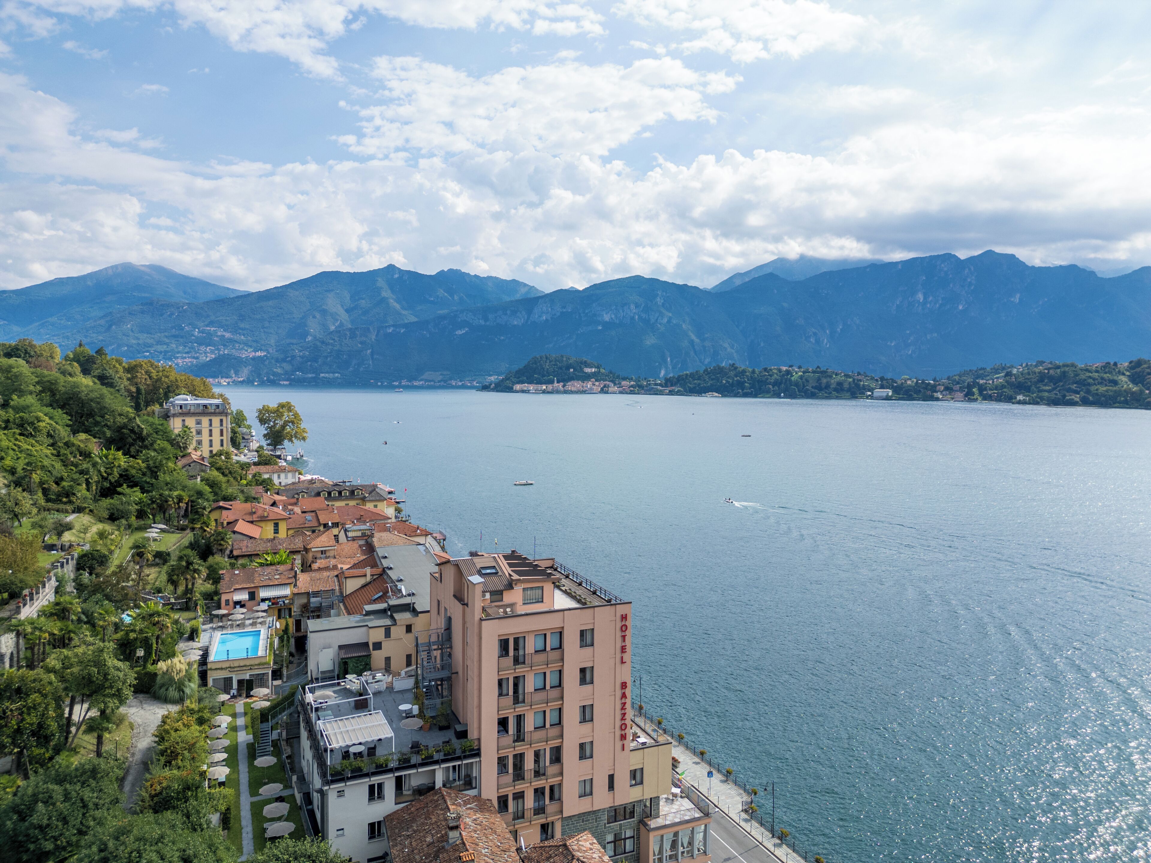 Un hotel con piscina, situato vicino a un lago con montagne sullo sfondo.