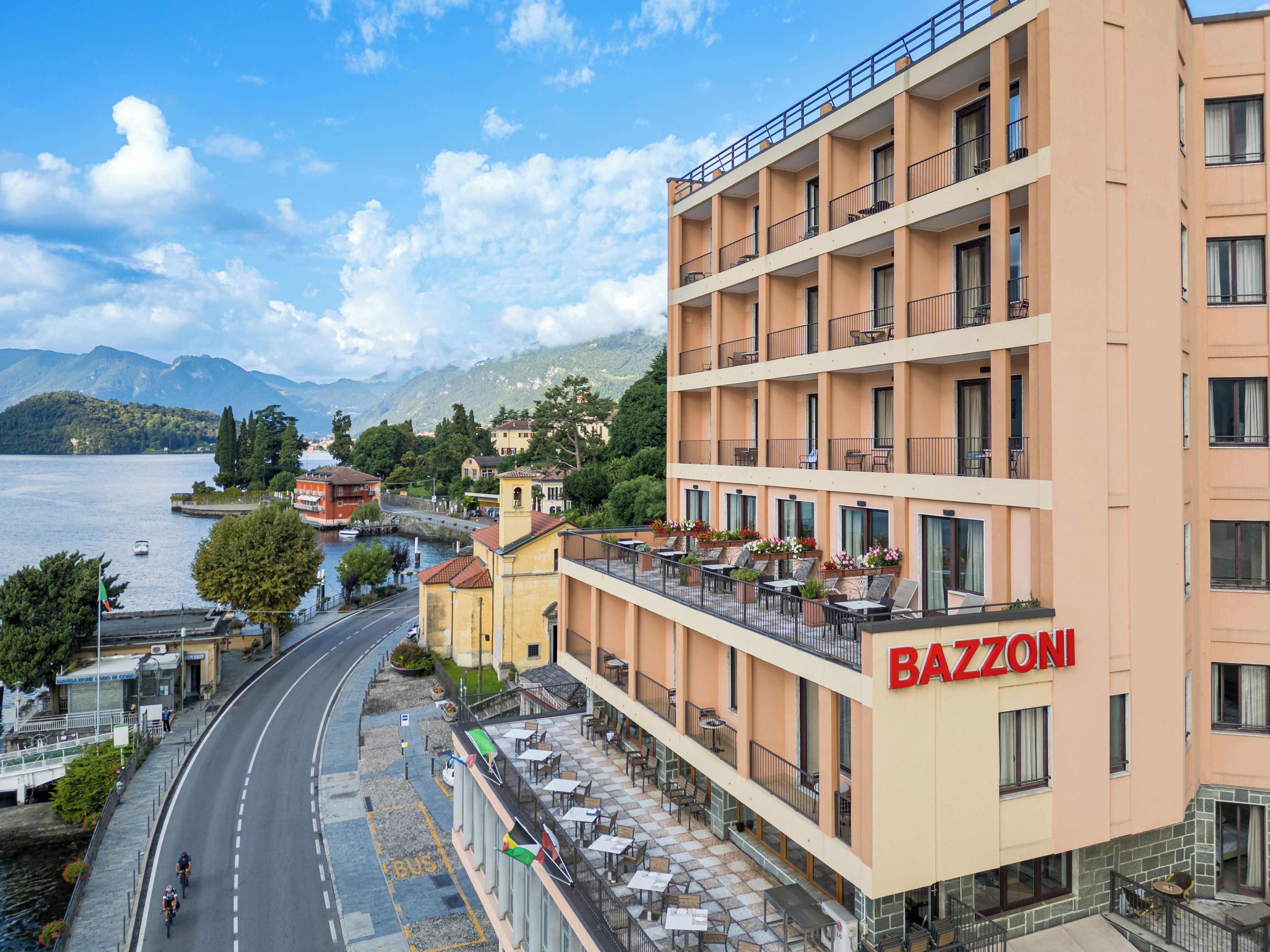 Hotel con vistas a un lago y montañas, con terraza exterior y un llamativo letrero "BAZZONI".