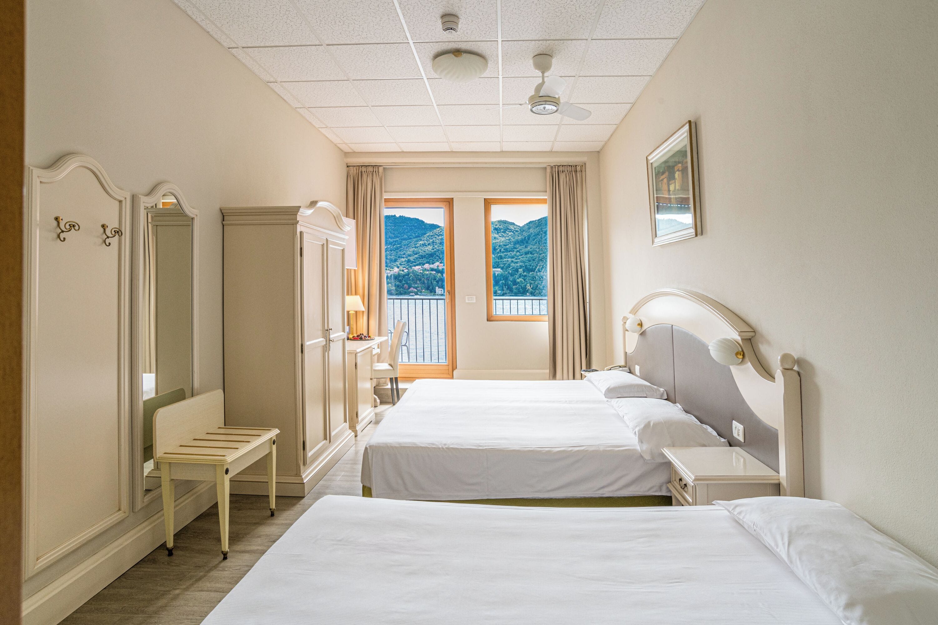 Ein Hotelzimmer mit zwei Betten, einer Bank, einem Kleiderschrank und einem Balkon mit Bergblick.
