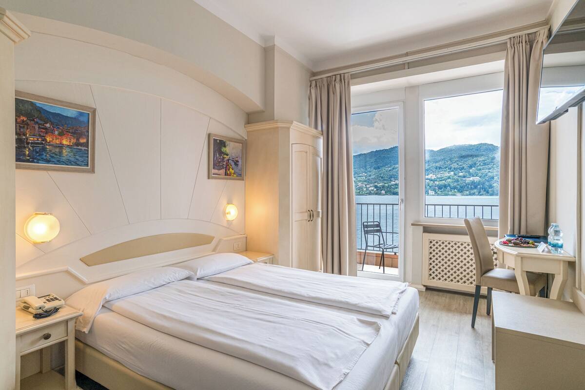 A hotel room with a bed, a desk, and a balcony with a view of the city.