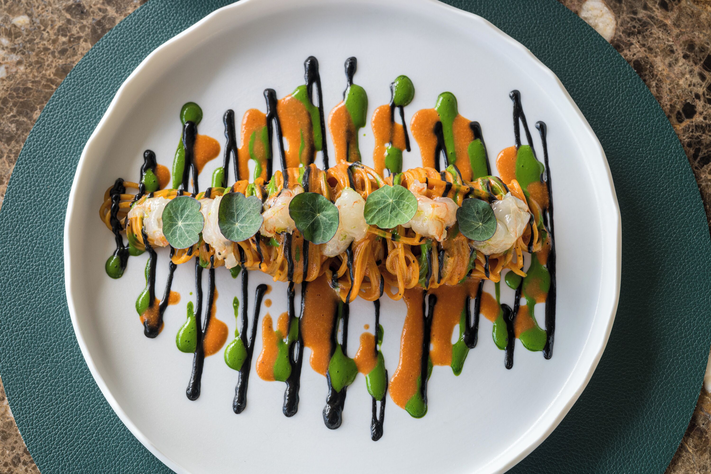 A white plate with a colorful dish, garnished with green leaves and drizzled with sauces.