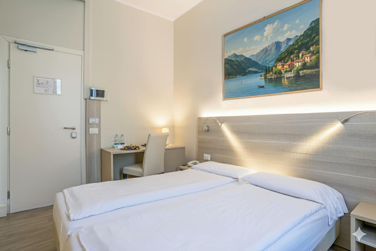 A hotel room with a bed, a desk, and a chair. There is a painting on the wall and a door with a sign.