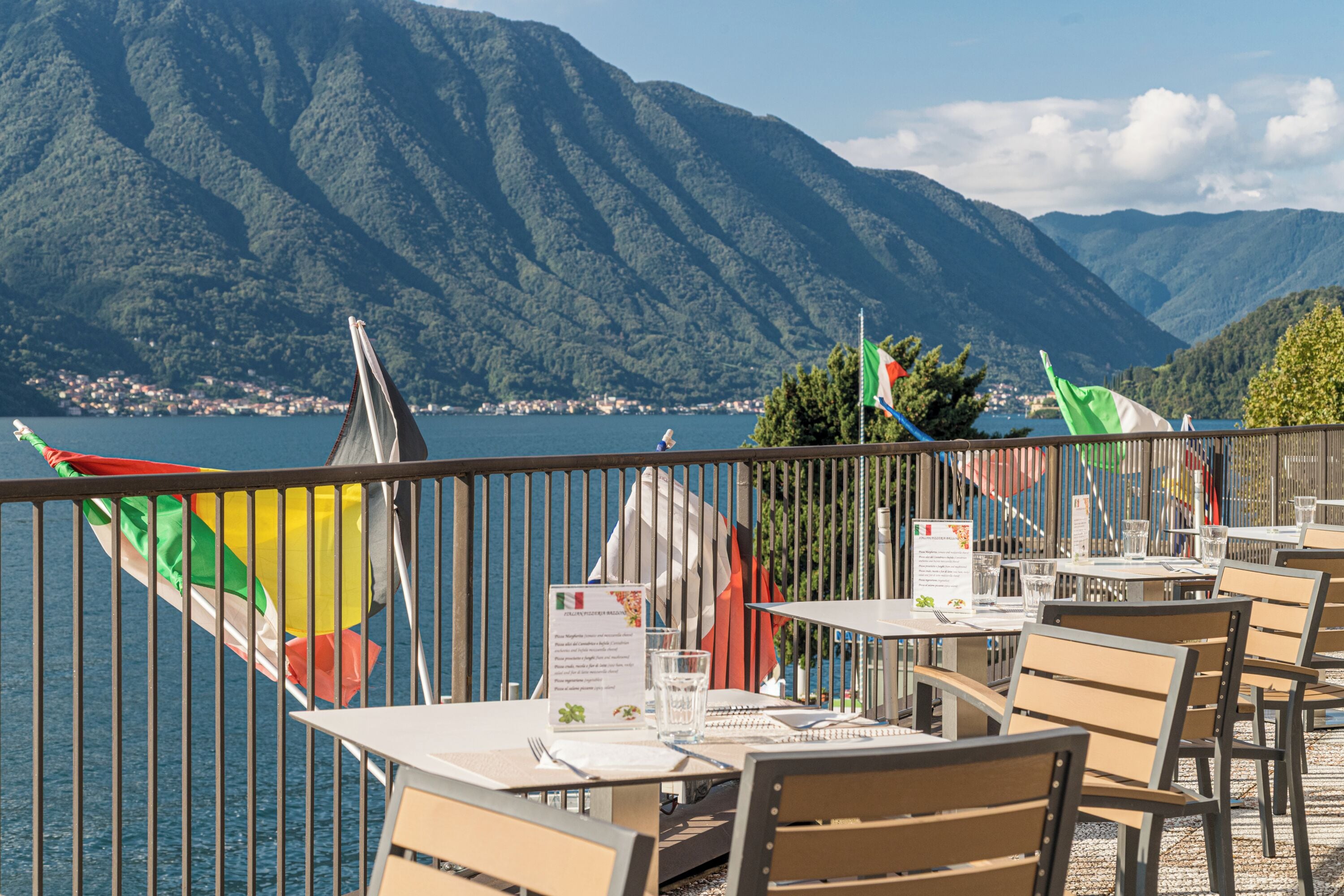 An outdoor dining area with tables and chairs, overlooking a lake and mountains.