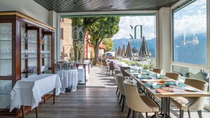 Un restaurante con una larga mesa dispuesta para comer, una vitrina con copas de vino y vistas a montañas a través de grandes ventanales.