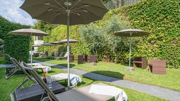 Un espace jardin aménagé avec des sièges d’extérieur, notamment des fauteuils et des tables, ainsi que des parasols pour créer de l’ombre.