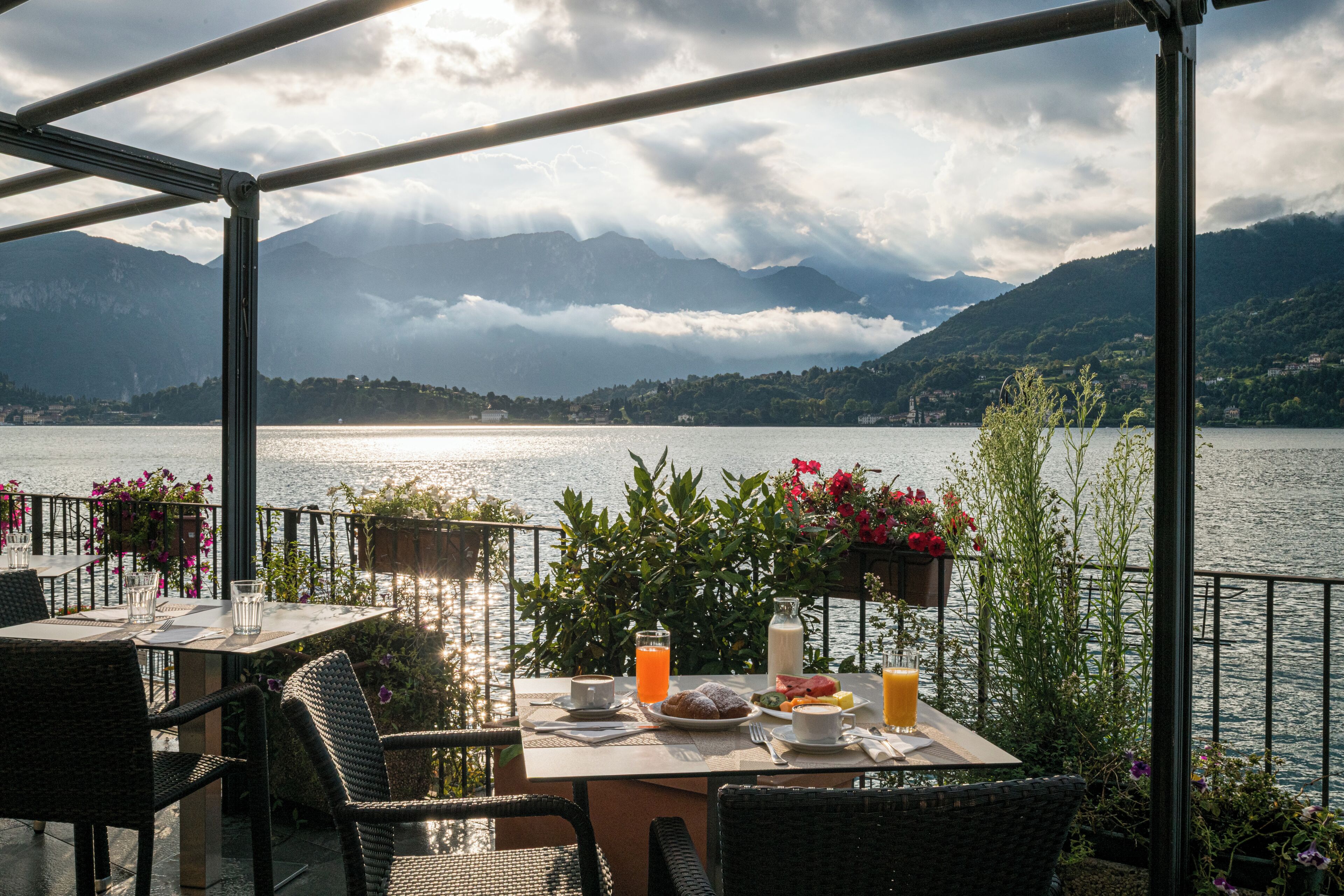 A terrace with a table set for breakfast overlooking a lake and mountains.