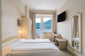 Quarto de hotel com duas camas, uma escrivaninha, uma cadeira, televisão e varanda com vista para as montanhas.
