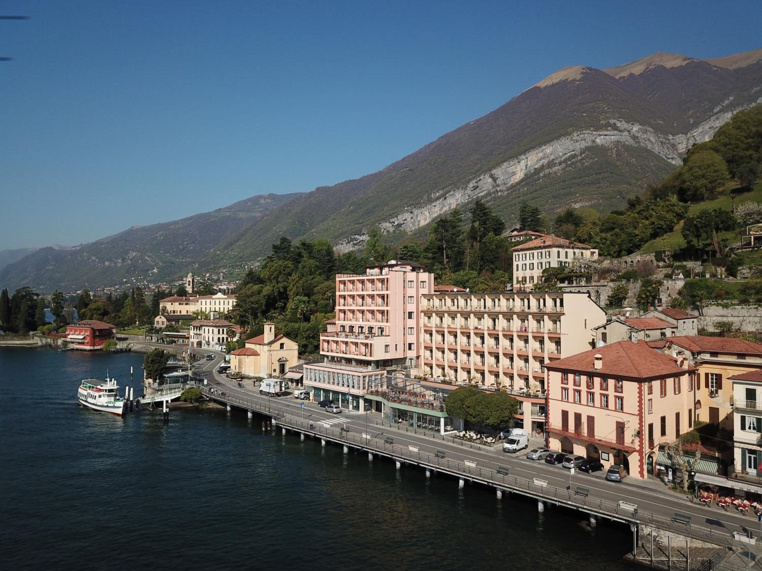 A waterfront hotel with a pier, buildings with balconies, and a mountainous backdrop.