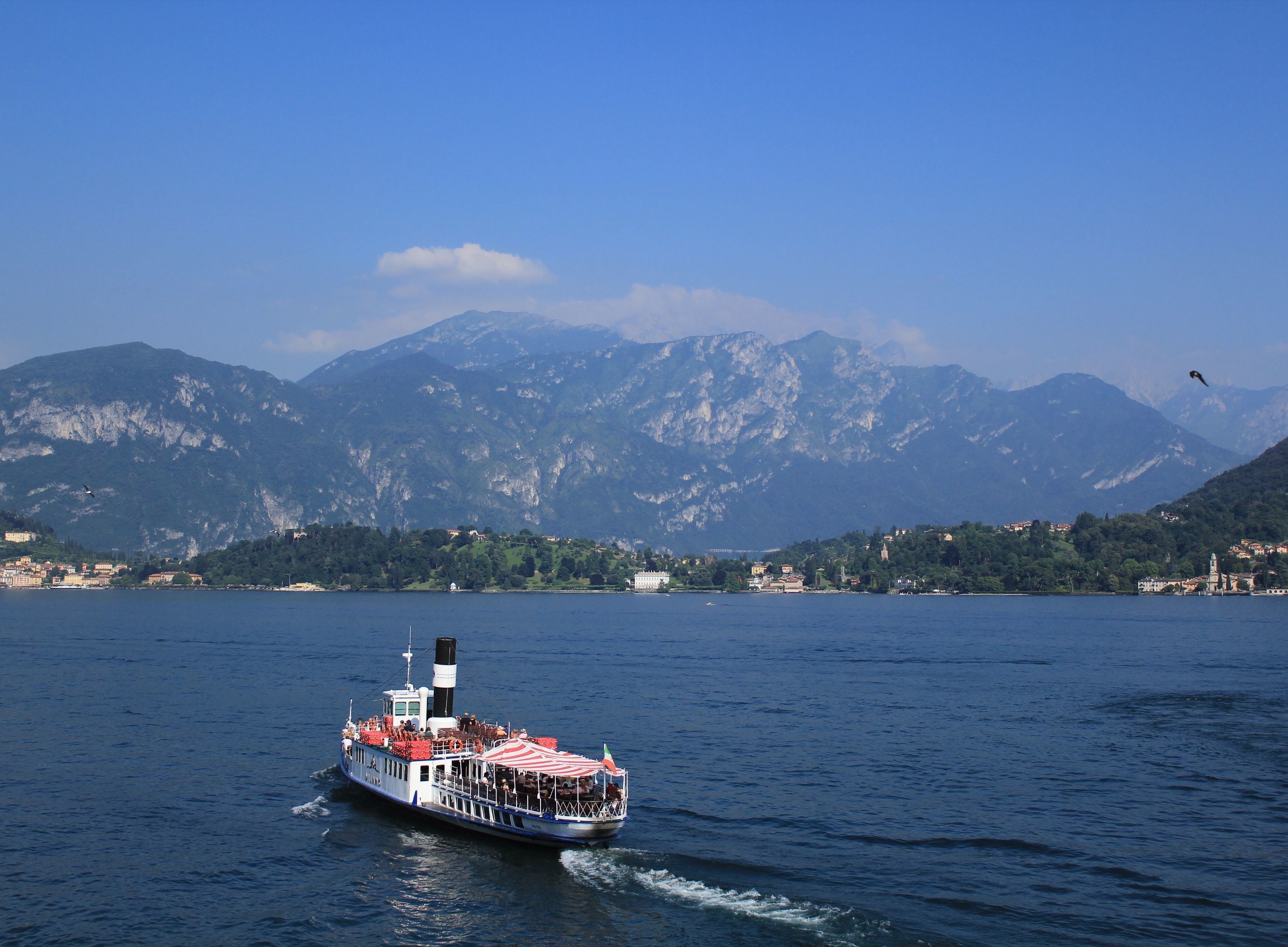 Una barca con un tetto a righe rosse e bianche che si muove su un lago, con montagne sullo sfondo.