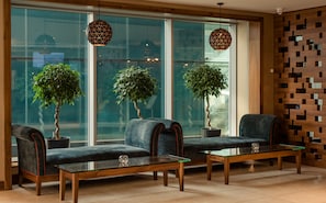 Un área de espera moderna con dos sillones tapizados en azul, una mesa con superficie de vidrio y plantas en macetas.