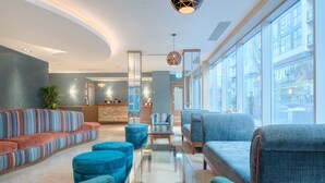 A modern lobby with a curved ceiling, a reception desk, and seating areas with blue upholstered sofas and ottomans.