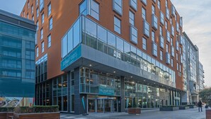 A modern hotel with a glass facade, a prominent entrance, and a sign reading "Tallaght Cross Hotel Dublin".