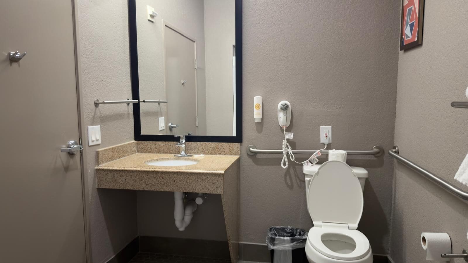 Et badeværelse med vask, spejl, toilet og håndtørrer.