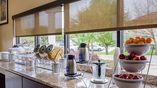 A buffet counter with various food items and beverages, a coffee maker, and a bowl of fruit. - Comfort Inn San Antonio Northeast (San Antonio)