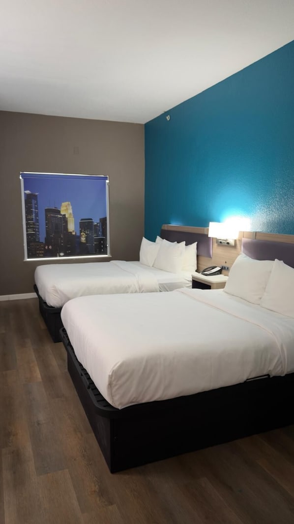 A hotel room with two beds, a cityscape view, a nightstand with a phone, and a blue accent wall.