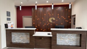 A reception desk with a wooden panel wall, a large C-shaped design, and a stone-textured counter. - Comfort Inn San Antonio Northeast (San Antonio)