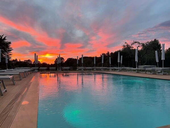 A swimming pool with lounge chairs and umbrellas, surrounded by trees, during sunset. - Miramonti (Fasano)
