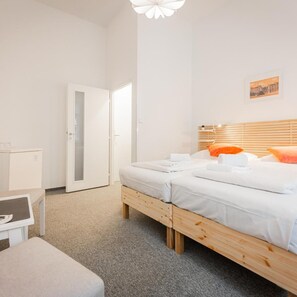 A hotel room with two beds, a desk, a chair, a wardrobe, and a door leading to another room. - Hotel Ostas (Prague)
