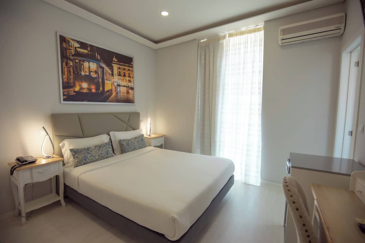 A neatly arranged bedroom with a large bed, bedside tables, a desk, and a painting on the wall.