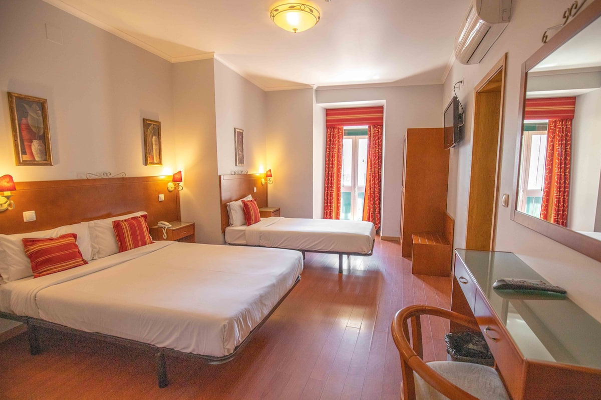 A hotel room with two beds, a desk, a chair, a TV, and a mirror.