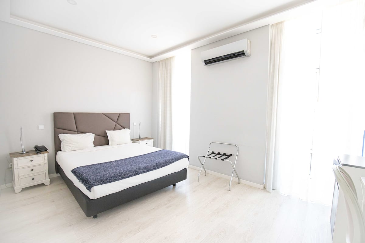 A modern bedroom with a large bed, bedside tables, a wall-mounted air conditioner, and a window with curtains.