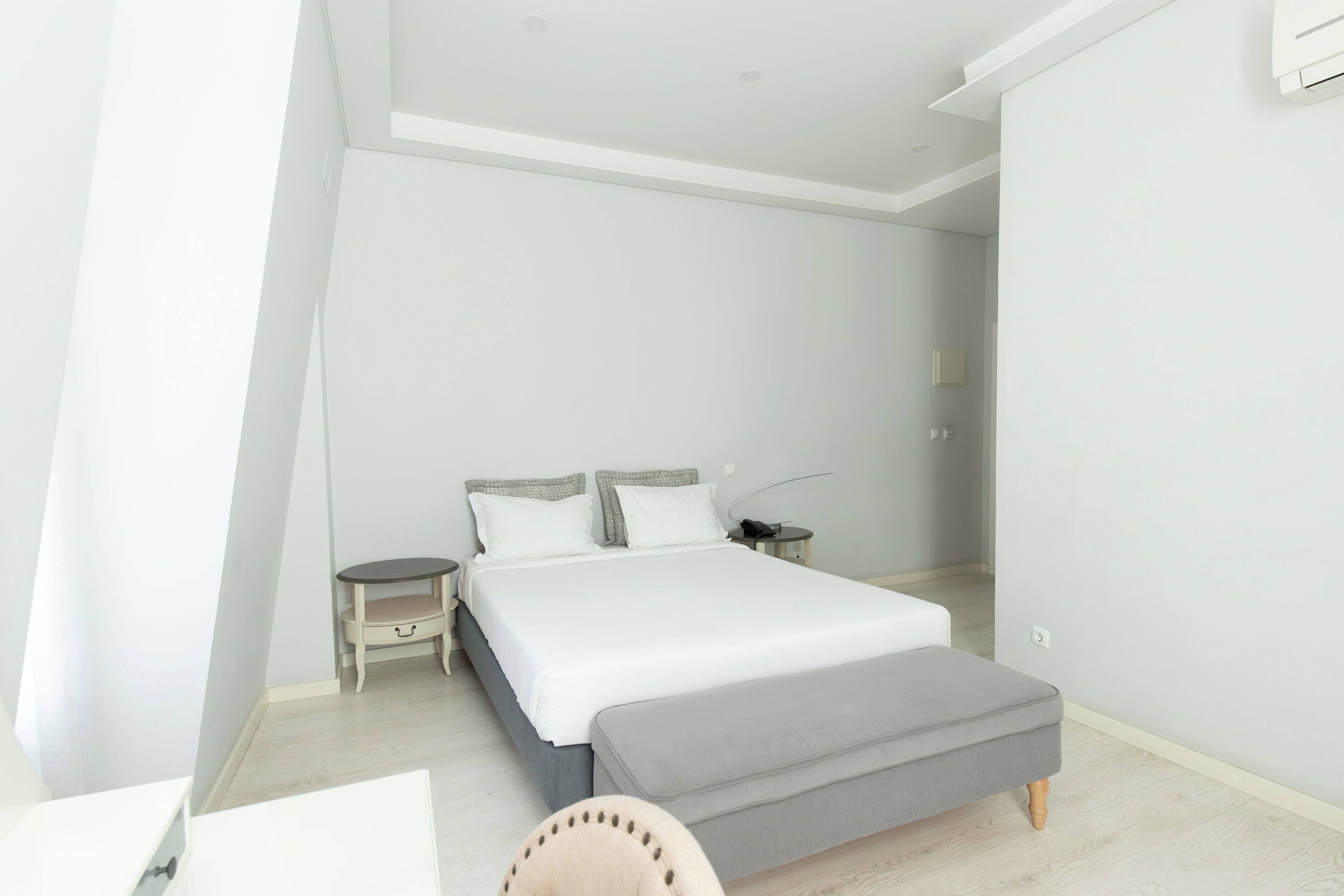 A modern bedroom with a large bed, bedside tables, a bench, and a desk.