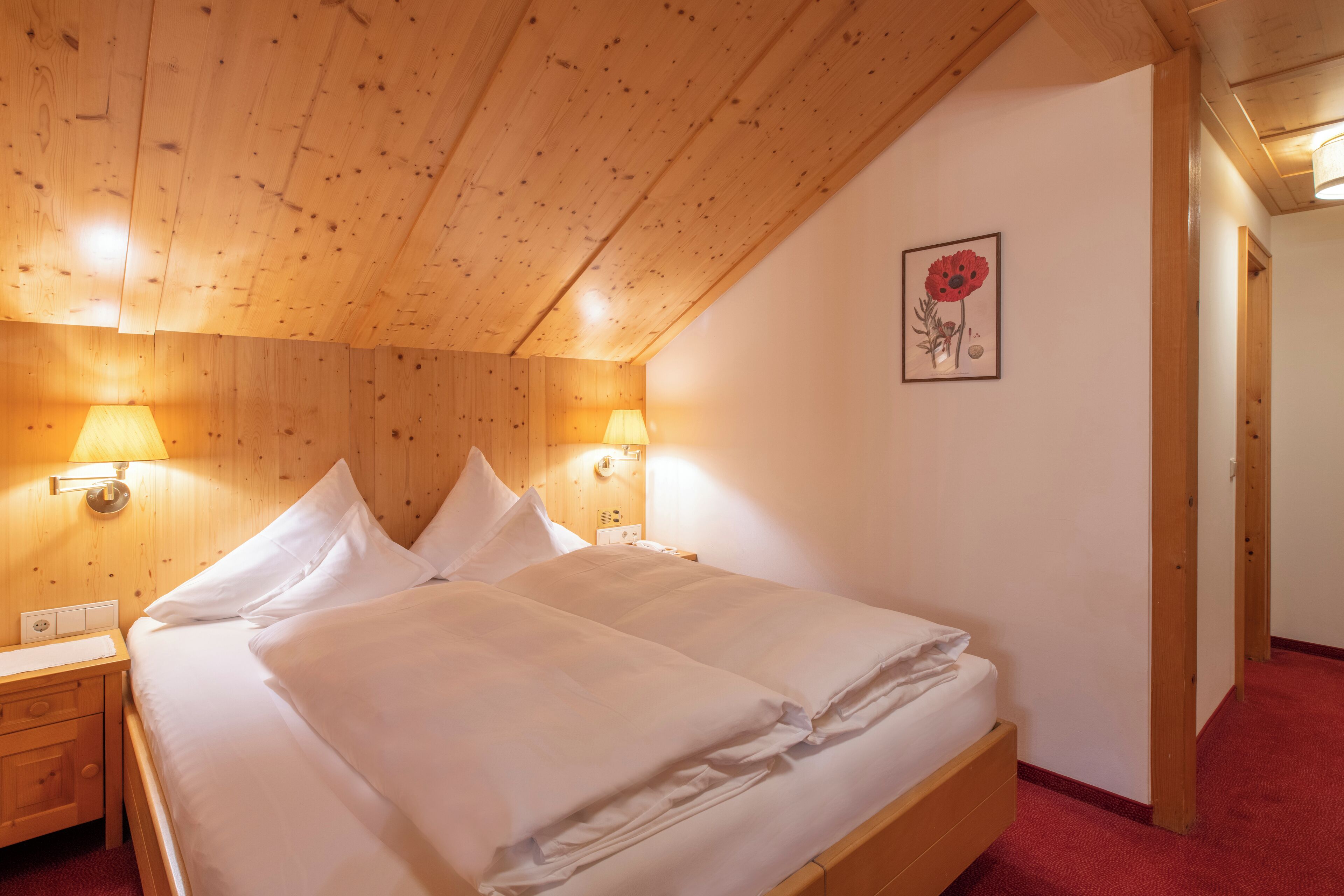 A neatly made double bed with white linens, wooden headboard, and two bedside lamps.