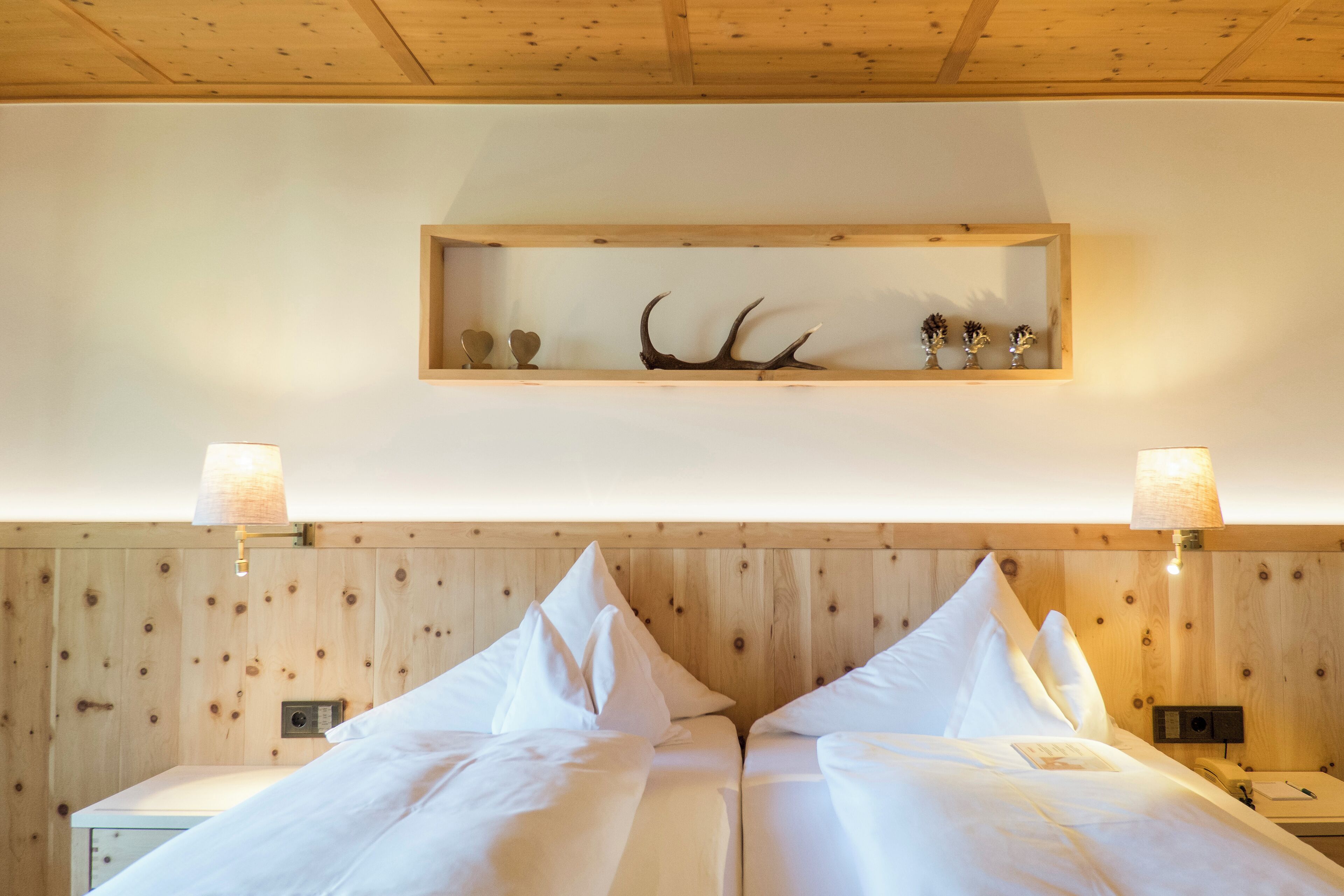 A room with two beds, wooden paneling, a shelf with antlers and vases, and bedside lamps.