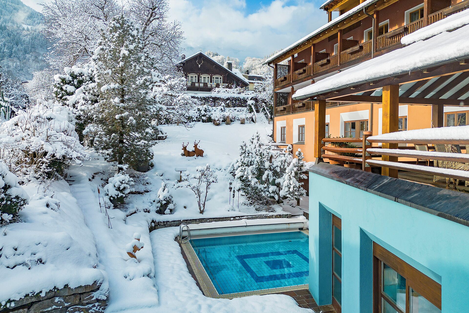 Un área de piscina exterior cubierta de nieve con una terraza de madera y un edificio con balcones.